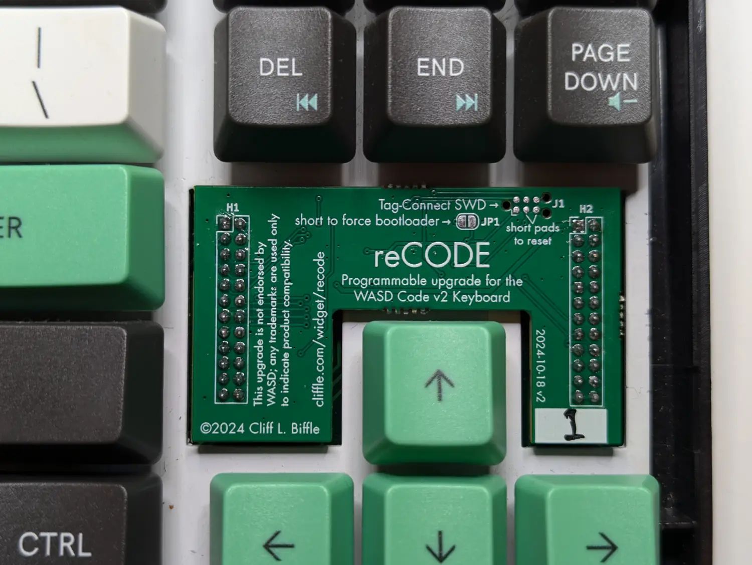 A green circuit board nestled between a keyboard’s arrow keys and its insert/delete cluster.